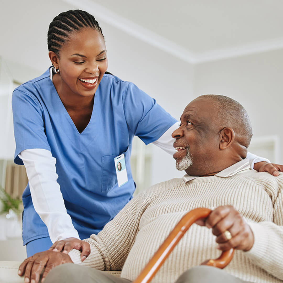 A nurse providing compassionate support to an older male patient using a cane during cancer care and recovery.
